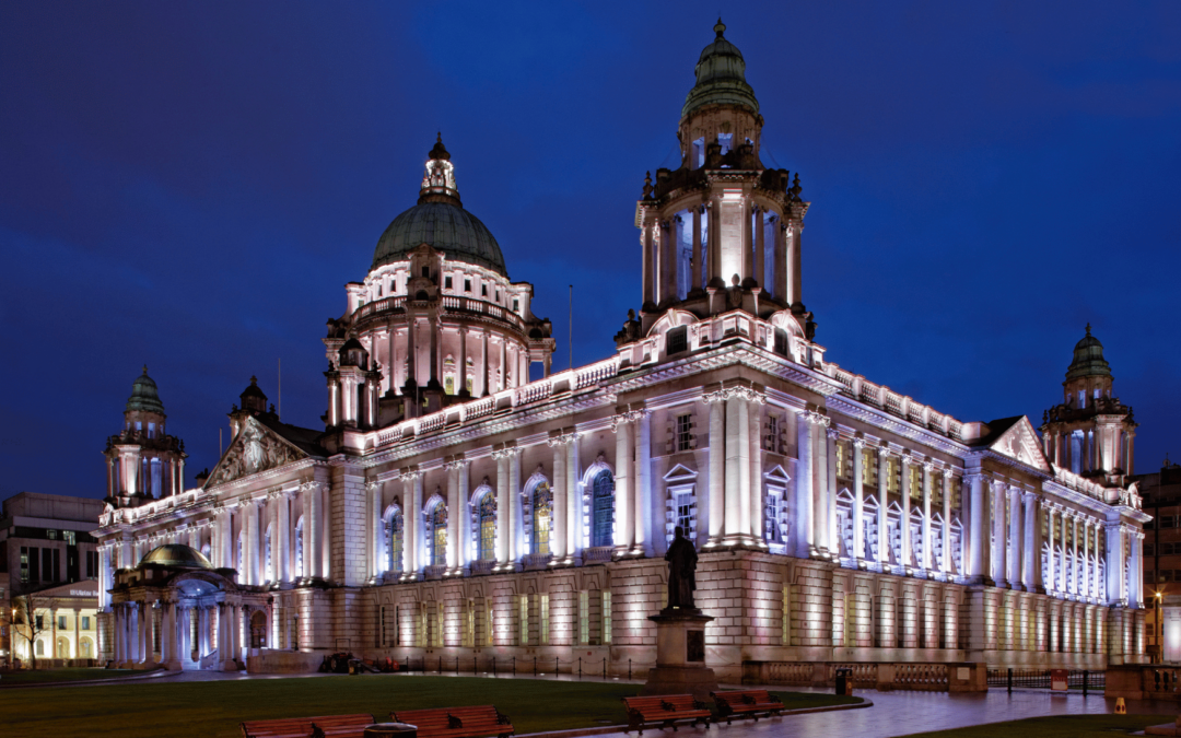 Belfast City Hall illuminated in purple light. It is nighttime.